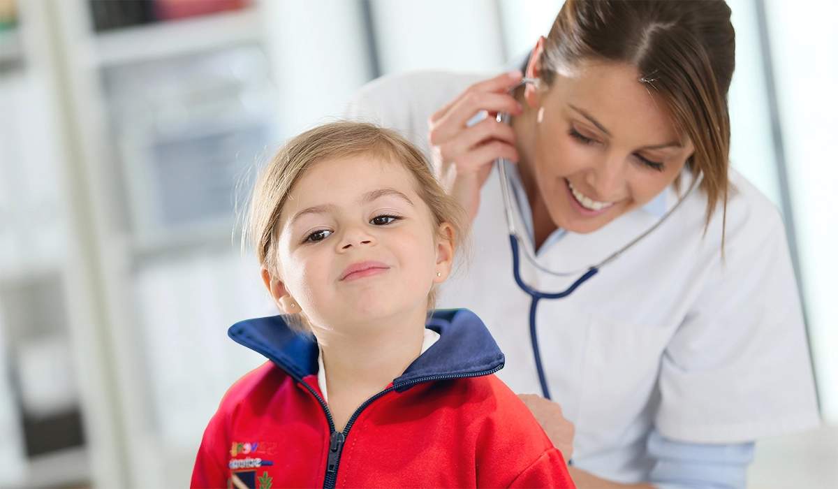 une petite fille dans une école maternelle est auscultée par un médecin