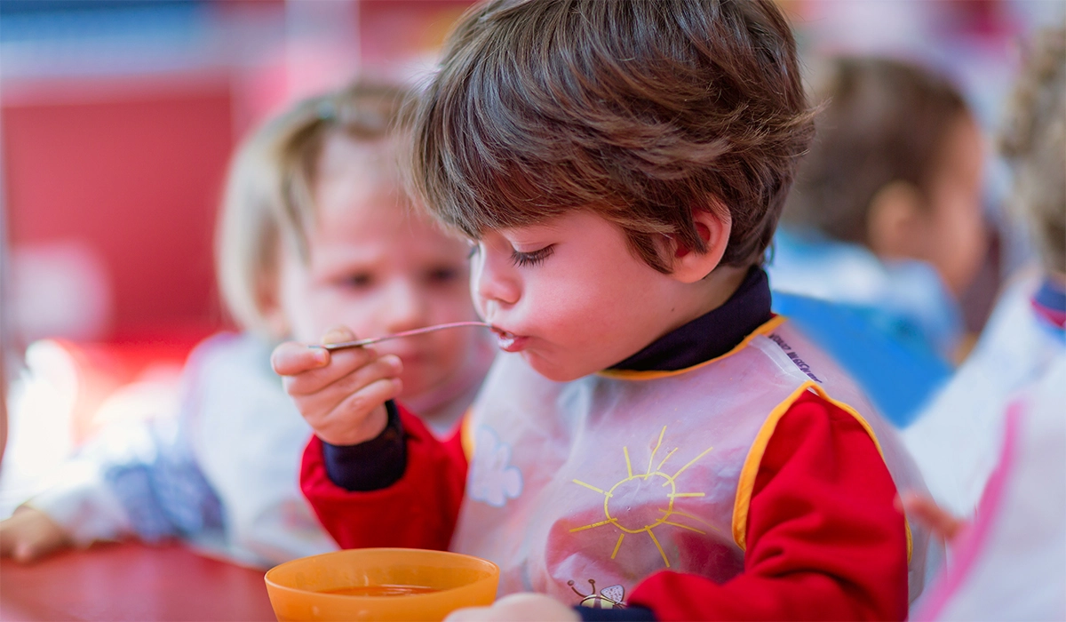 enfant en bas âge à l'école maternelle mangeant de manière autonome à la cantine