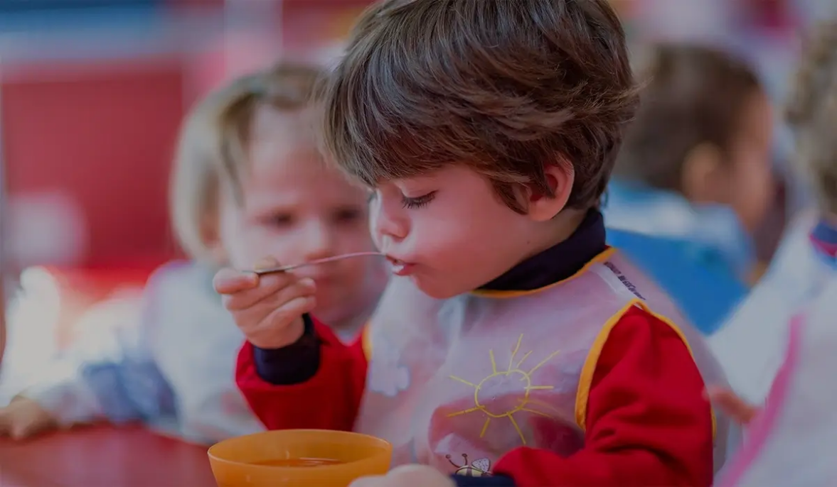 niño pequeño de escuela infantil comiendo de modo autonomo en el comedor